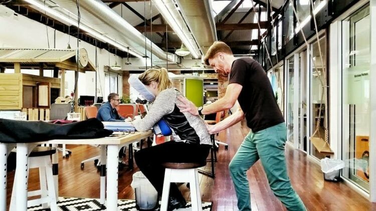 A man gives a woman an office massage in an open plan office space