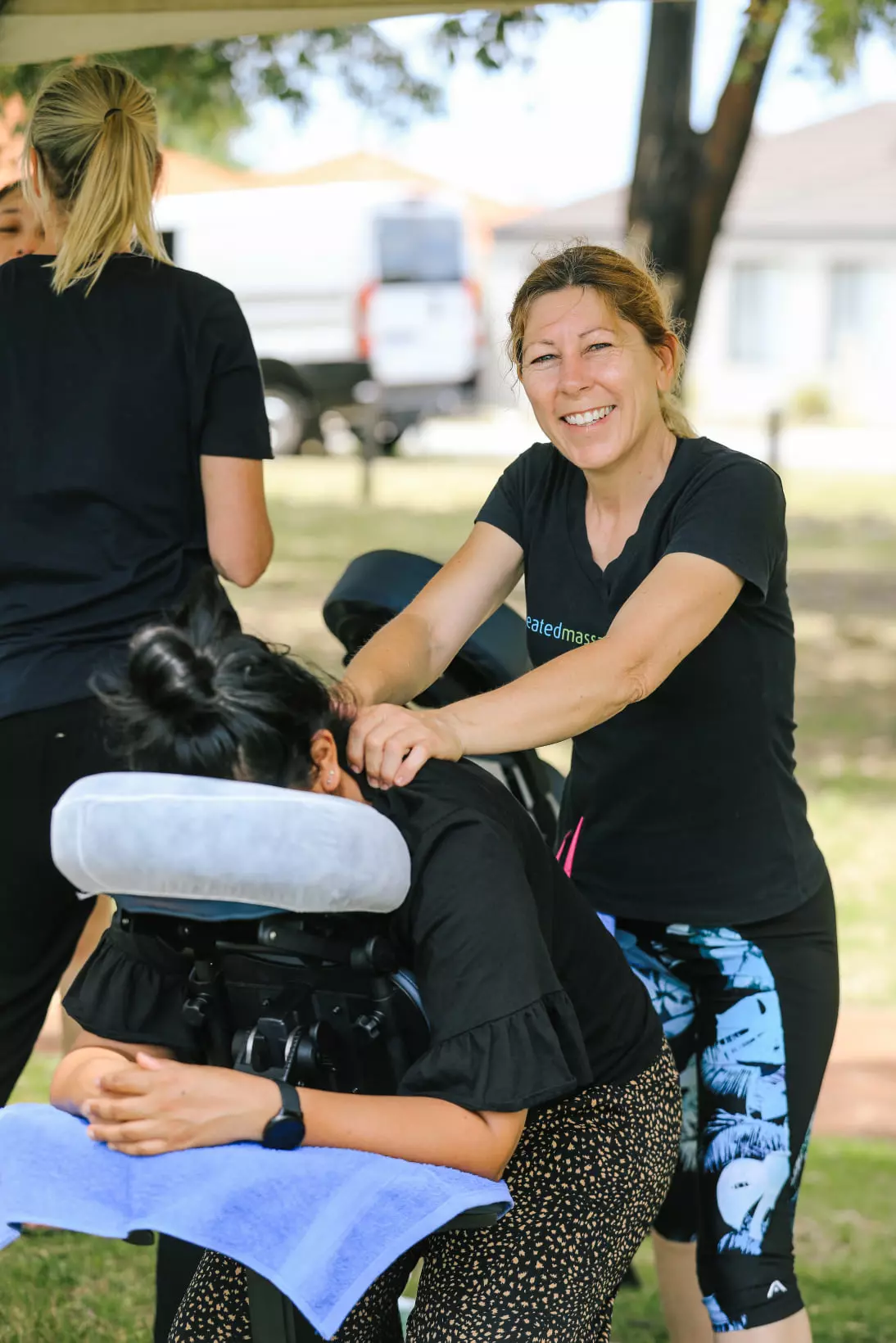 A female massage therapist giving a massage outdoors at an event and smiling at the camera
