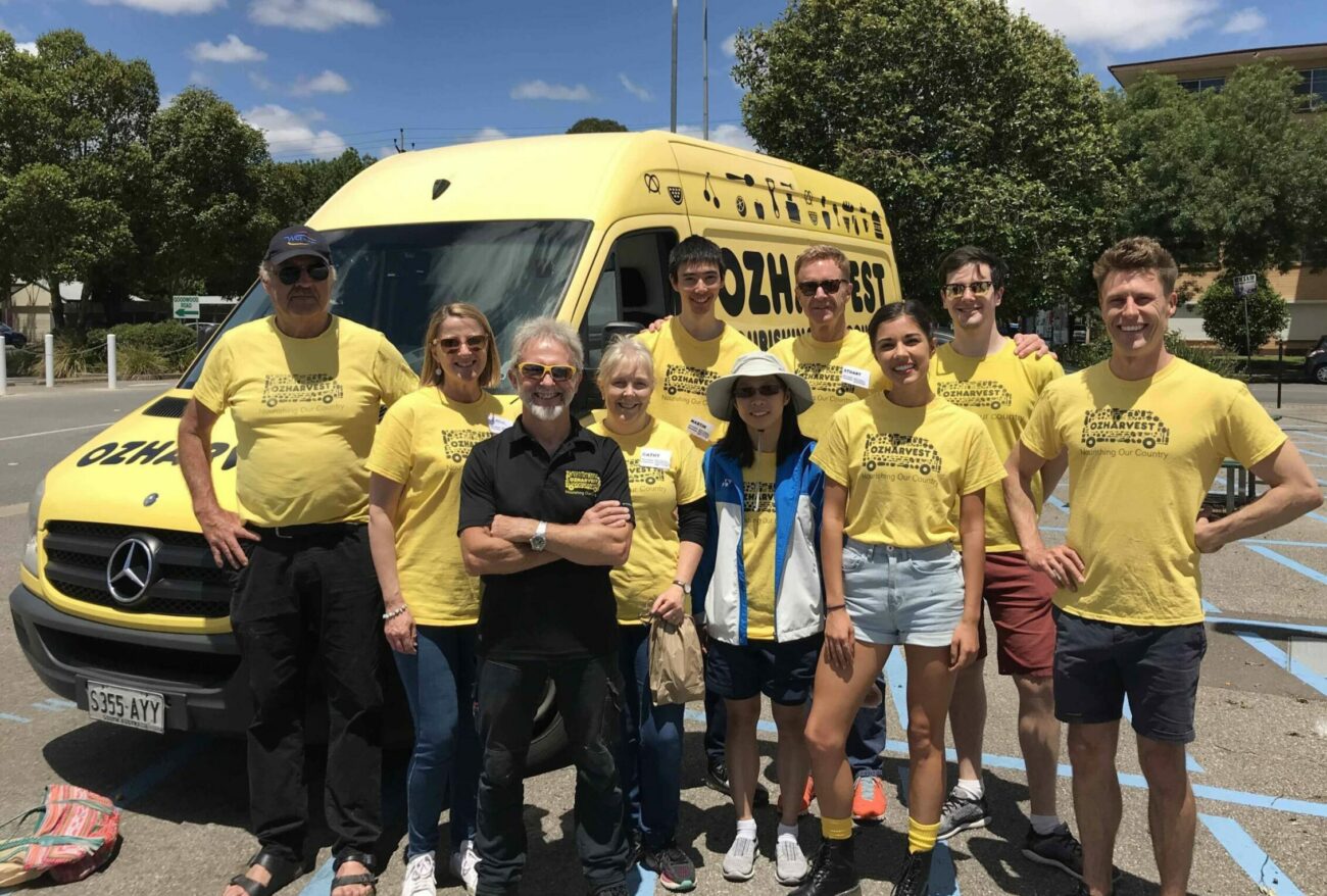 A group of volunteers wearing yellow tshirts standing with an OzHarvest van