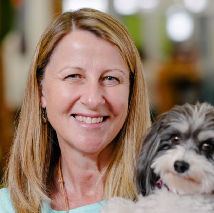 A woman with blonde hair smiles at the camera while holding a cute dog