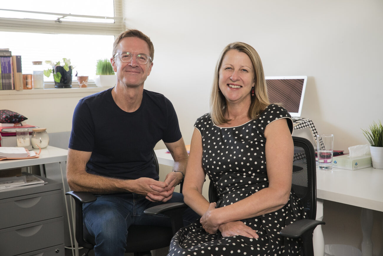 A man and woman sitting in their office, smiling at the camera