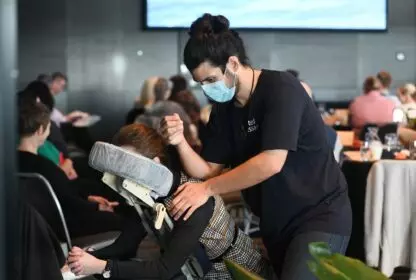 A massage therapist wearing a face mask giving a chair massage at a conference